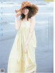 A woman in a yellow dress and straw hat on the beach.