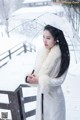 A woman in a white coat holding an umbrella in the snow.